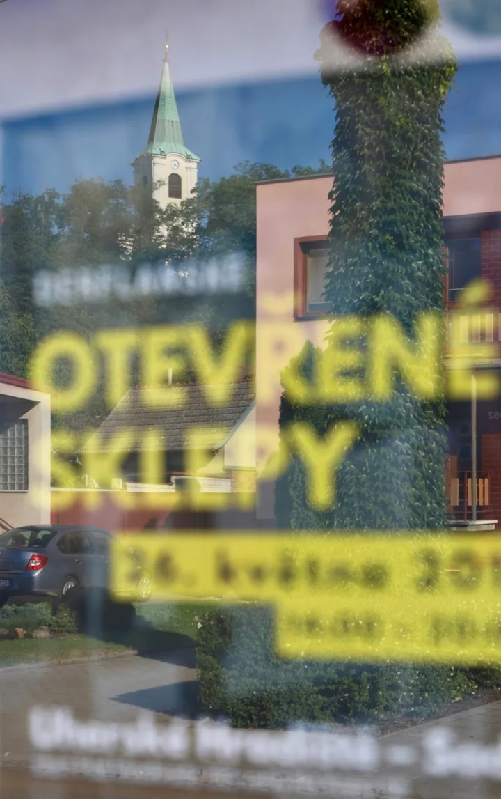 Plakát Derflanských otevřených sklepů za sklem, v odrazu kostelík a domy v Sadech